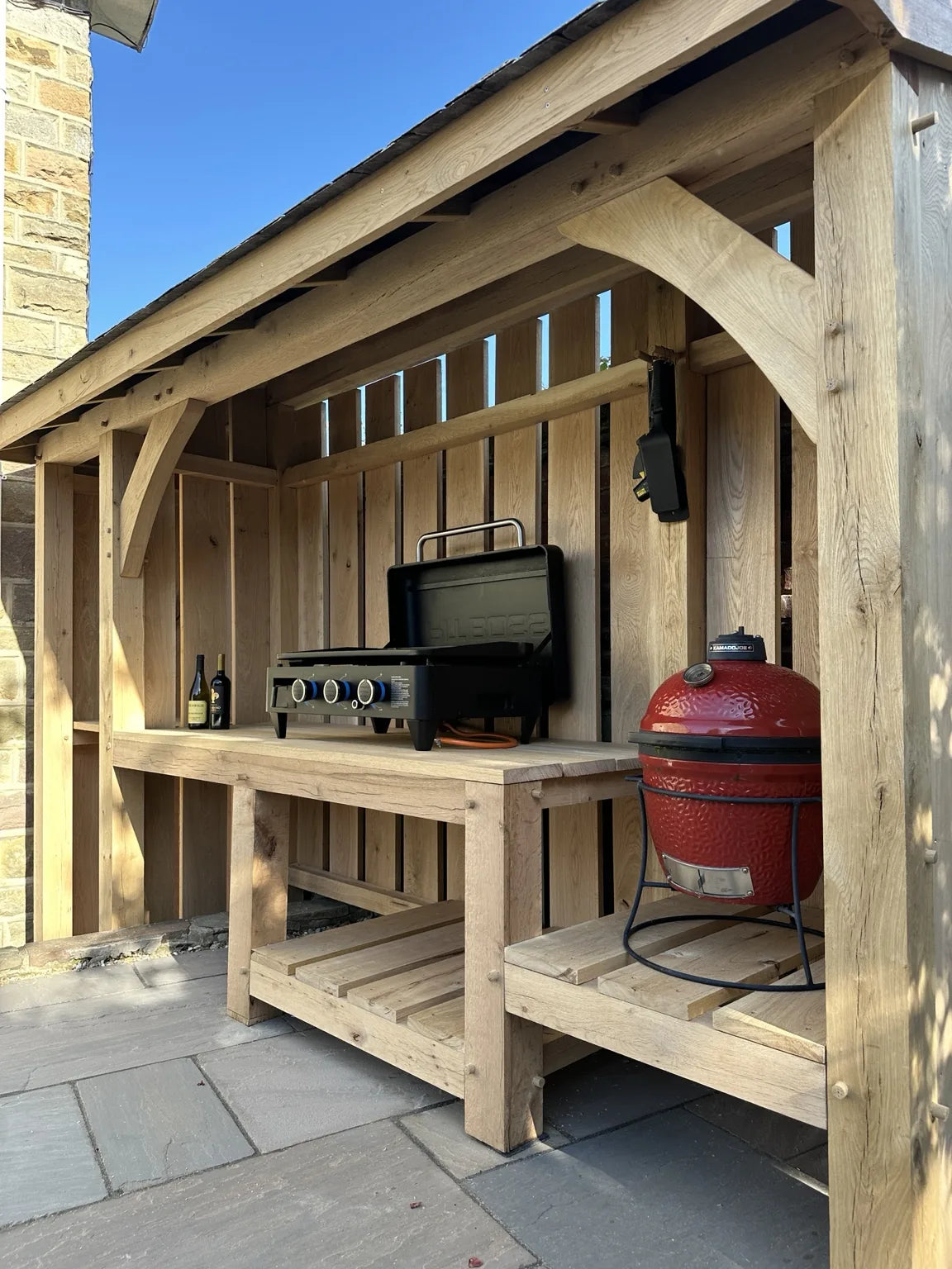 Bespoke oak outdoor kitchen and BBQ shelter with curved braces, timber worktops and a red ceramic barbecue